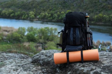 Backpack with camping mat and trekking poles on rocky hill, space for text