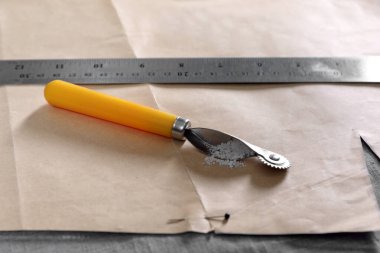 Kumaşta dikiş deseni olan izleme tekerleği ve cetvel, yakın plan.