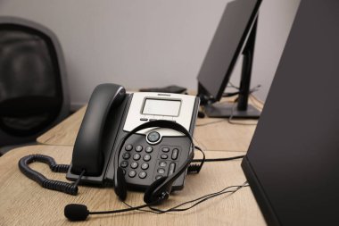 Ofisteki ahşap masada sabit telefon ve kulaklık. Yardım hattı servisi
