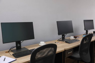 Ofisin içini aç. Açık gri duvarın yanında bilgisayarları olan modern işyerleri