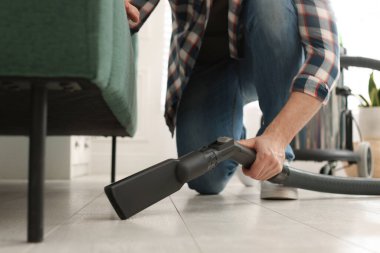 Man vacuuming floor under sofa in living room, closeup