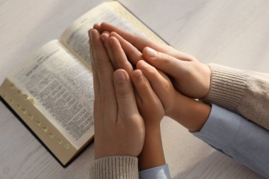 Oğlan ve vaftiz ebeveyni birlikte beyaz tahta masada dua ediyorlar.