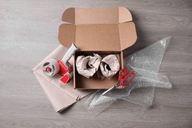 Paketlenmiş eşyalar, yapıştırıcı bant, makas, kağıt ve baloncuk ambalajlı kutuyu ahşap masaya aç, düz uzan