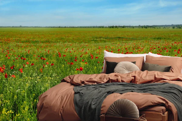 Comfortable bed with soft pillows in in poppy field on sunny day