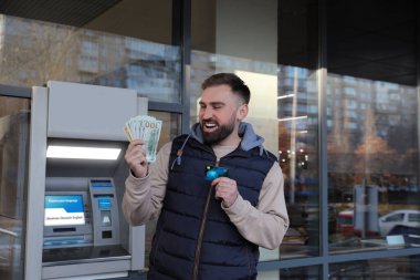 Açık hava bankasının yanında kredi kartı ve parası olan heyecanlı bir adam.