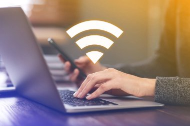 Akıllı telefon ve dizüstü bilgisayar kullanan bir kadın kapalı bir masadaki Wi-Fi 'ye bağlanıyor.