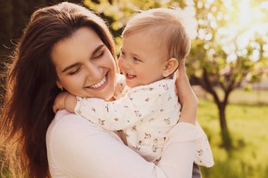 Güneşli bir günde parkta sevimli bebeğiyle mutlu bir anne.