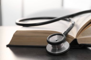 Kapalı alandaki gri masada öğrenci ders kitabı ve steteskop açık. Tıp eğitimi