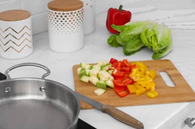 Ahşap tahta, kesilmiş sebzeler ve bıçakla mutfak tavasının yanında.