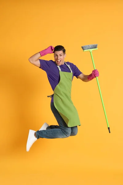绿色扫帚在橙色背景上跳跃的男人 — 图库照片