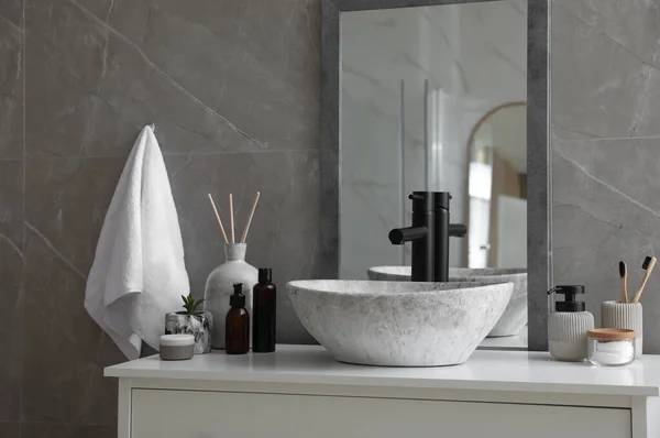 Stone vessel sink with faucet and toiletries on white countertop in bathroom