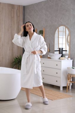 Banyoda yumuşak beyaz bornoz giyen güzel bir genç kadın.