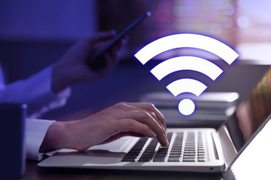 Laptop kullanan ve Wi-Fi 'ye bağlı akıllı telefon kullanan bir kadın.