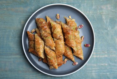 Açık mavi ahşap masada fıstıklı enfes bir baklava.