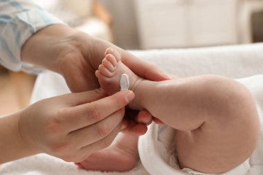 Anne, küçük bebeğine iç mekanda vücut kremi sürüyor.