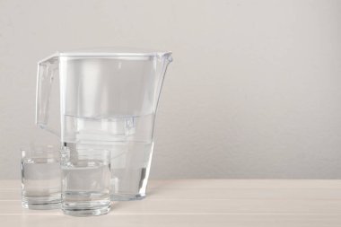 Süzgeç testisi ve cam bardaklar beyaz masada, arka planda saflaştırılmış su ile. Metin için boşluk