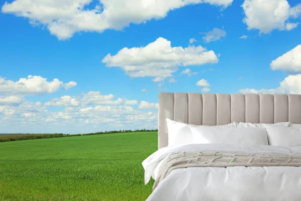Comfortable bed with soft pillows in green field on sunny day