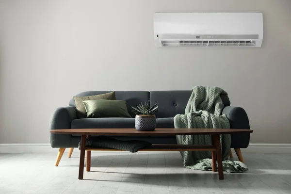 Modern air conditioner on light grey wall in room with stylish sofa