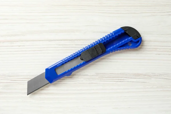 Blue utility knife on white wooden table, top view. Construction tool