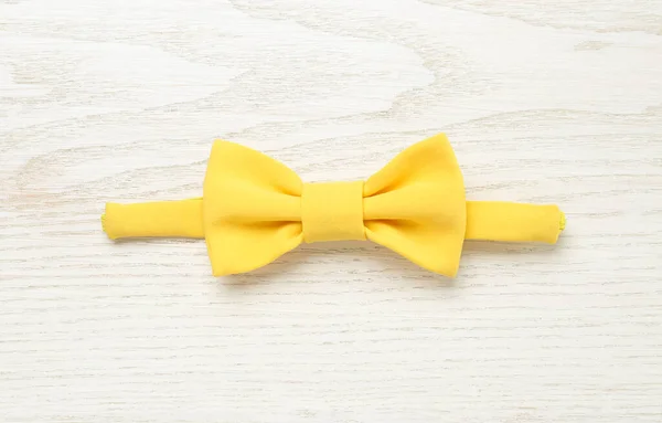 Stylish yellow bow tie on white wooden background, top view