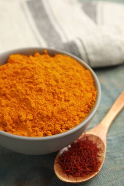 Bir kase safran tozu ve kaşık açık mavi ahşap masada kurumuş çiçek lekeleri.