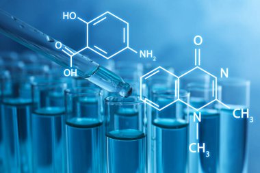 Test tüpüne mavi arka planda sıvı damlatılıyor, yakın plan.