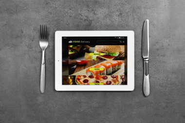 Çevrimiçi yemek siparişi için açık sayfası olan modern tablet ve siyah masa üzerinde çatal bıçak takımı. Teslimat hizmeti kavramı
