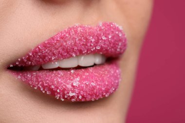 Dudakları şekerle kaplı genç bir kadın, pembe arka planda, yakın plan.