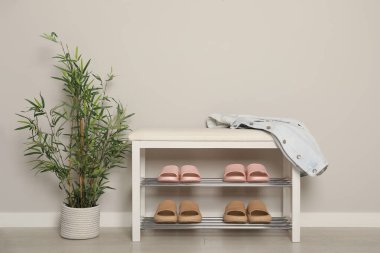 Farklı çift lastik terlikleri olan şık bir depolama tezgahı ve koridordaki beyaz duvarın yanında güzel bir bitki örtüsü.
