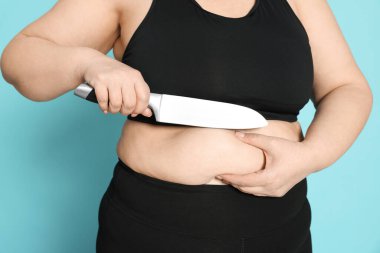Açık mavi arka planda bıçaklı obez kadın, yakın plan. Kilo kaybı ameliyatı