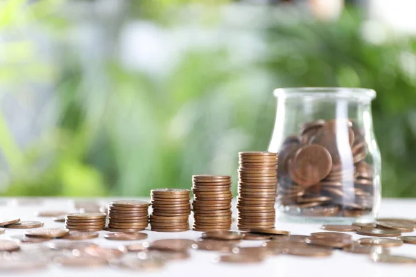 Glasburk Och Metall Mynt Vitt Bord Mot Suddig Grön Bakgrund — Stockfoto