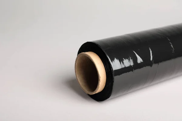 Roll of black stretch wrap on light grey background, closeup. Space for text