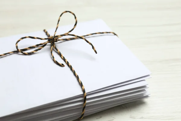 Stack of letters tied with string on white wooden table, closeup