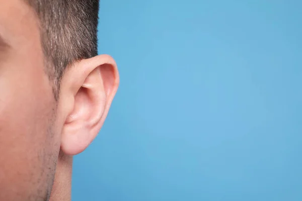 Man on light blue background, closeup of ear. Space for text