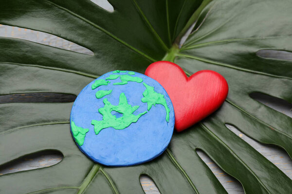 С Днем Земли. Планета из пластилина и декоративного сердца на зеленом листе, крупным планом