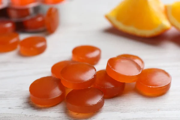 Many orange cough drops on white wooden table, closeup