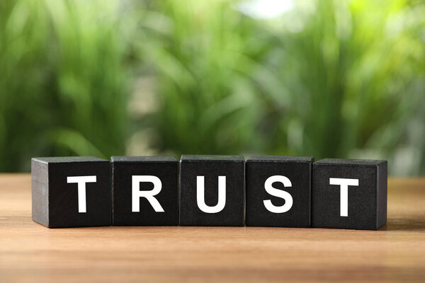 Word Trust made of black cubes on wooden table against blurred background