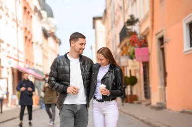 Şehir caddesinde birlikte yürüyen kahve bardakları olan sevimli genç bir çift. Romantik randevu
