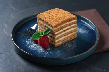 Siyah masada servis edilen nane, ahududu ve pudra şekerli lezzetli katmanlı ballı kek.
