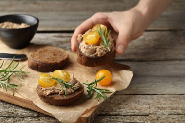 Ahşap masadan lezzetli ezmeli ve domatesli bir dilim ekmek alan kadın, yakın plan.