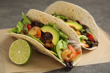 Gri masada karidesli lezzetli tacolar, avokado ve limon, yakın plan.