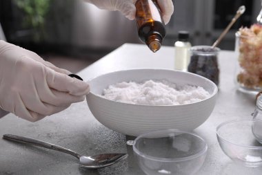 Eldivenli kadın, gri masadaki banyo bombasına gerekli yağı ekliyor, yakın plan.