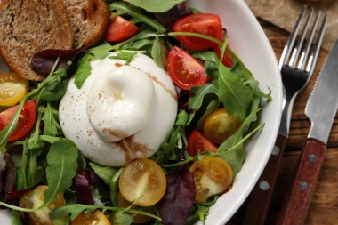 Ahşap masada servis edilen renkli domatesli, kızarmış ekmek ve roka soslu nefis burata salatası.