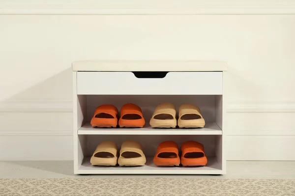 Stylish storage cabinet with different pairs of rubber slippers near white wall in hall