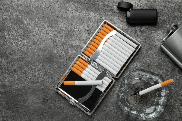 Öppen Låda Med Tobaksfiltercigaretter Tändare Glasaskfat Och Fickkolv Grått Bord — Stockfoto