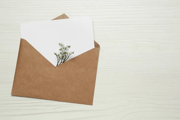 信封上有空白的纸制卡片和白色木制桌子上的花朵 顶视图 案文的篇幅 — 图库照片
