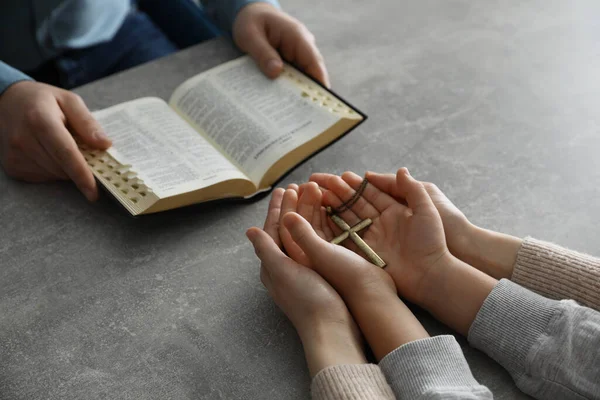 男孩和他的教父教母在灰暗的桌子边祷告和阅读圣经 — 图库照片