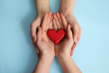 Genç ve yaşlı kadınlar açık mavi arka planda kırmızı kalp tutuyorlar.