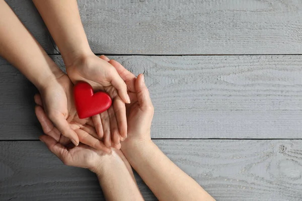 Genç ve yaşlı kadınlar, gri ahşap masada kırmızı kalp taşıyorlar. Metin için boşluk