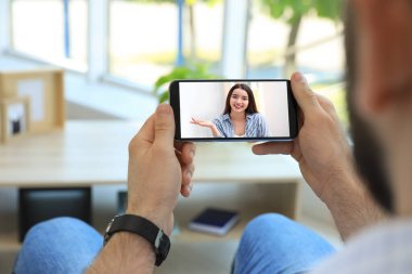 Güzel bir kadınla konuşan bir adam akıllı telefondan görüntülü konuşma yapıyor. Kapalı alanda. Online randevu